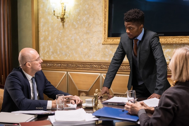 Mature man and woman looking at their young african male colleague