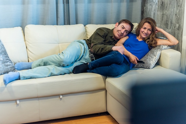 Mature man and woman lying on the couch watching a movie. High quality photo