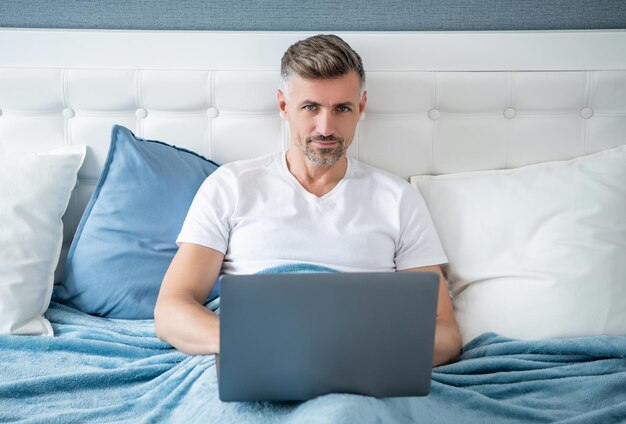 Mature man working on computer in bed