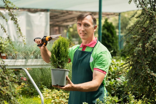 Photo mature man working in garden center standing and holding pot plants