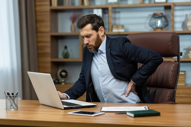 Mature man working in modern office with laptop senior boss having severe back pain businessman at