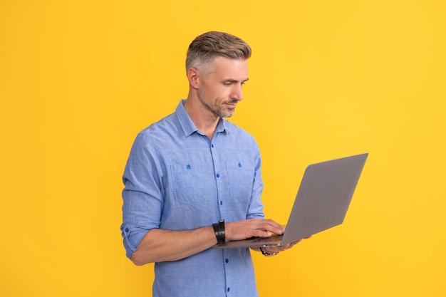 Mature man working online on laptop on yellow background business