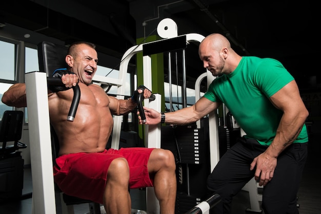 Mature Man Working Out In Gym  Doing Chest Exercise On Machine With Help Of His Trainer