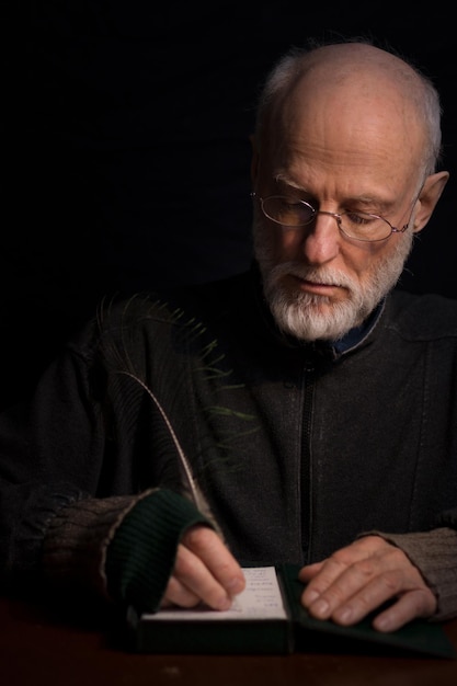 mature man writing in paper at table against black background