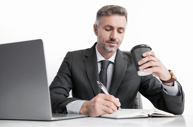 Mature man writing at the table in business office and drinking coffee