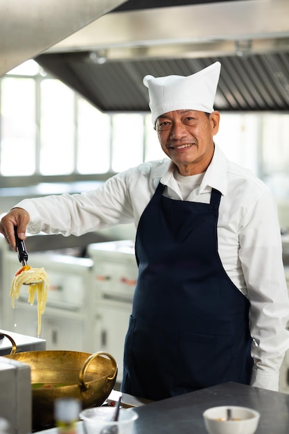 Mature master chef looking at camera Cooking class portrait senior asian thai male professional chef cooking meal culinary classroom cooking school cooking lessons in a cooking school