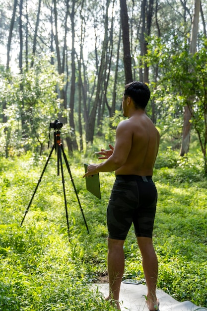 Mature middleaged athlete man standing in stand position in
sporty clothes on fitness mat watching video training tutorial
online vlogging