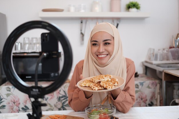 Foto donna musulmana matura in hijab che mangia pane in cucina