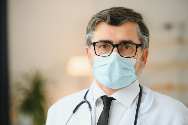 Mature old medical healthcare professional doctor wearing white coat stethoscope glasses and face mask Medical staff health care protection concept Portrait