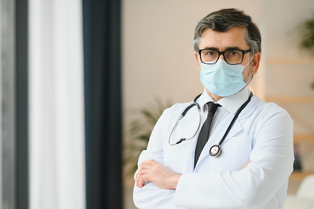 Зрелый старый медицинский профессиональный врач в белом халате, стетоскоп, очки и маска для лица Медицинский персонал Концепция защиты здравоохранения Портрет