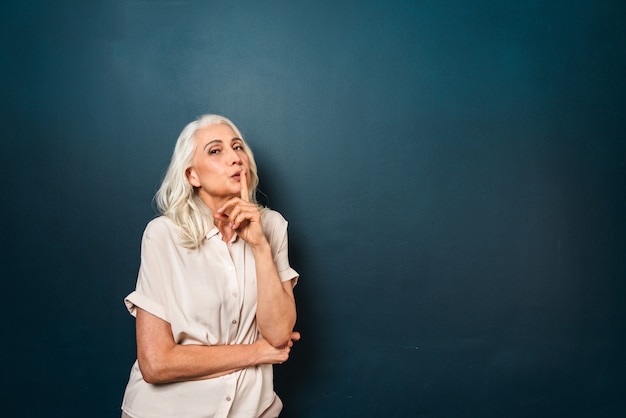 Photo mature old woman showing silence gesture.