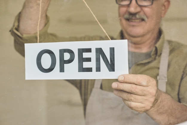 Mature owner of store or cafe putting open signboard on the door