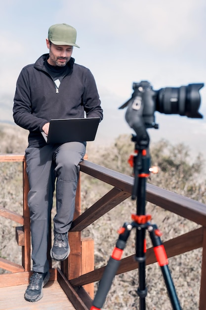 Mature person with a laptop and photographic camera sitting on lookout point working over the pacific ocean portrait