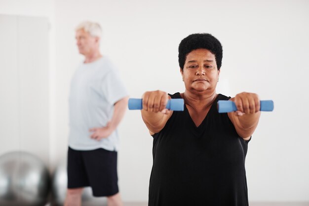 Mature plump woman exercising with dumbbells during sports training in the class