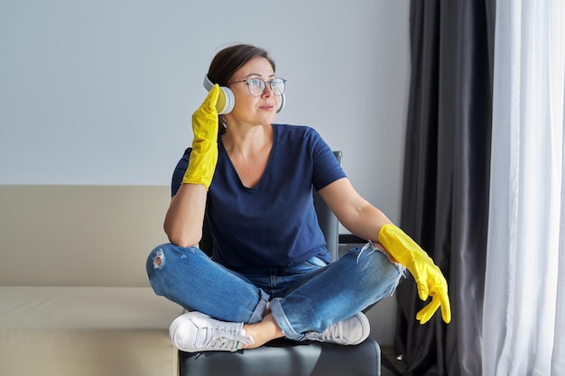 家の掃除をしているヘッドフォンゴム手袋の成熟したポジティブな女性。人、家事、ハウスキーピングのコンセプト