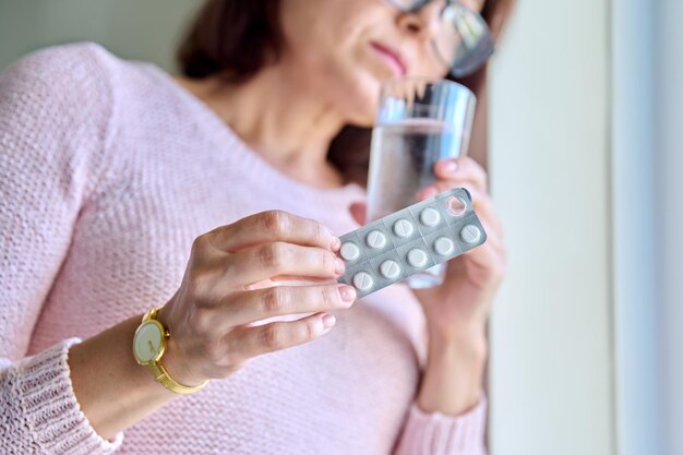 Photo mature sad woman with blister of pills and glass of water at home