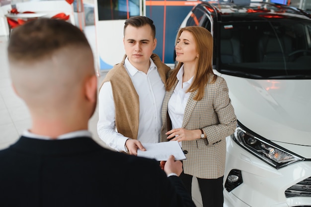 Mature salesman showing new car to a couple in showroom