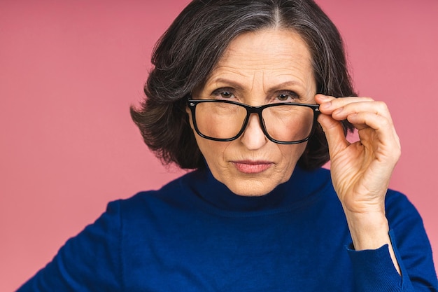 Mature senior aged serious or angry old woman isolated over pink background.