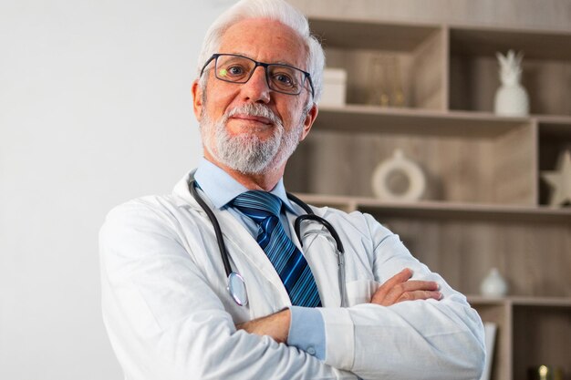 Зрелый старший врач-мужчина в медицинской форме в очках улыбается, глядя в камеру в больнице или у врача