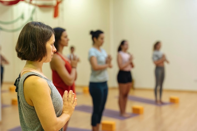 Mature shorthaired woman practicing yoga samasthiti pose with\
more women