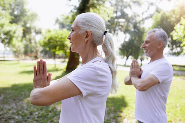 Photo mature smiling couple meditating while keeping their palms together