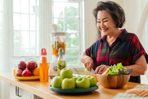 성숙한 웃는 여자 요리 샐러드 과일과 야채 집에서 신선한 녹색 과일 샐러드와 매력적인 성숙한 여자 집 주말 시간에 휴식 부엌 카운터에 서 수석 여자 앞치마