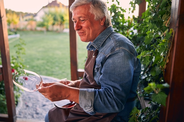 Mature sommelier in a winery garden sitting alone and looking at the empty glass after drinking wine