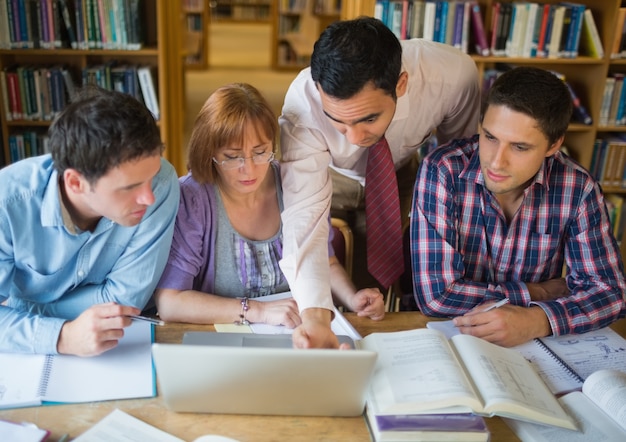 Studenti maturi con l'insegnante e il computer portatile in biblioteca