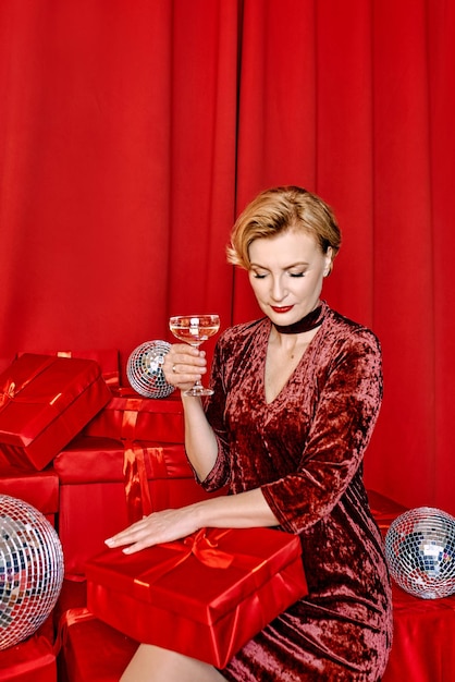 Mature stylish elegant woman with glass of sparkling wine with present on red background.