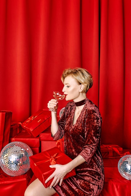 Mature stylish elegant woman with glass of sparkling wine with present on red background.