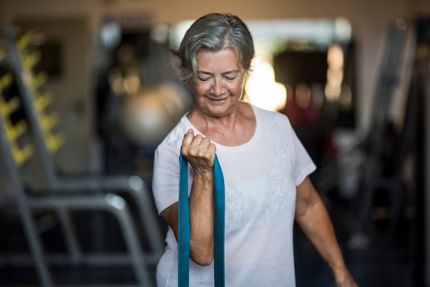 Donna matura da sola in palestra che fa esercizi con un elastico - stile di vita e concetto sano e fitness - anziano o pensionato che la lavora in salute