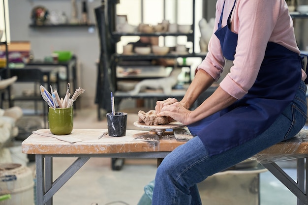 Mature woman in apron shaping, creating clay ceramics in pottery workshop studio