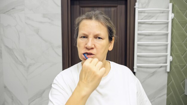 зрелые в ванной Зрелая женщина чистит зубы с усталым выражением в ванной комнате | Премиум  Фото