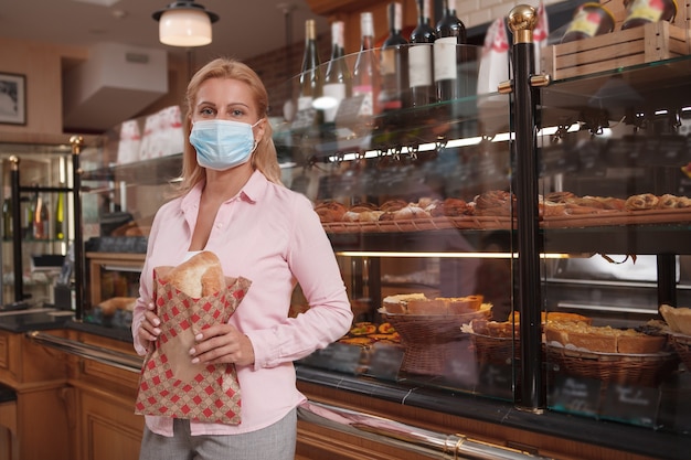 Donna matura che compra il pane durante una pandemia di coronavirus, indossa una maschera