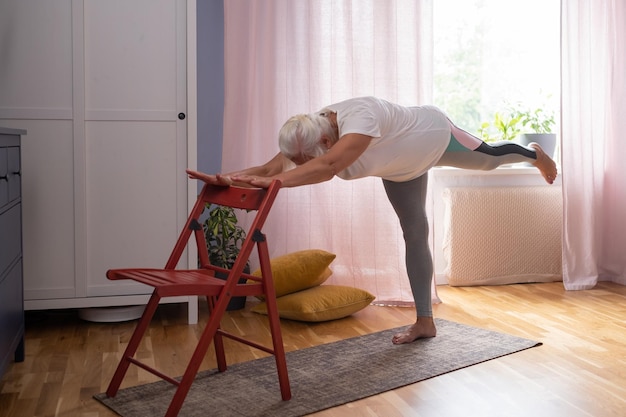 Donna matura in abiti casual che si esercitano a casa a praticare yoga