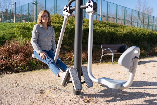 公共の公園の体操器具で足を使ってエクササイズをしている成熟した女性