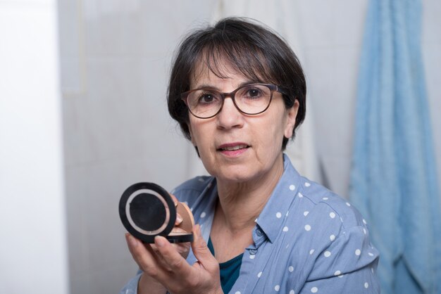 Mature woman doing makeup while looking at small mirror