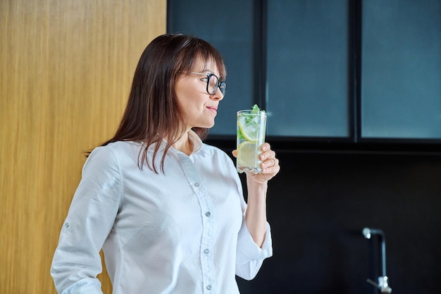 Mature woman drinking glass of water with lemon ice mint