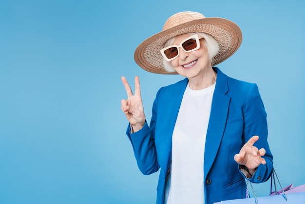 Зрелая женщина наслаждается хорошими покупками с сумками в руках, изолированными на синем фоне
