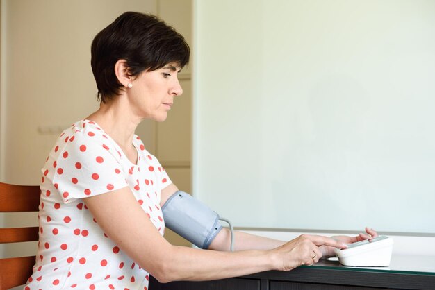 Photo mature woman examining blood pressure at home