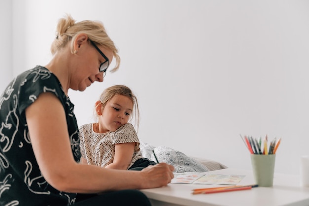 Mature woman granny with grandchild preschool girl drawing together at home