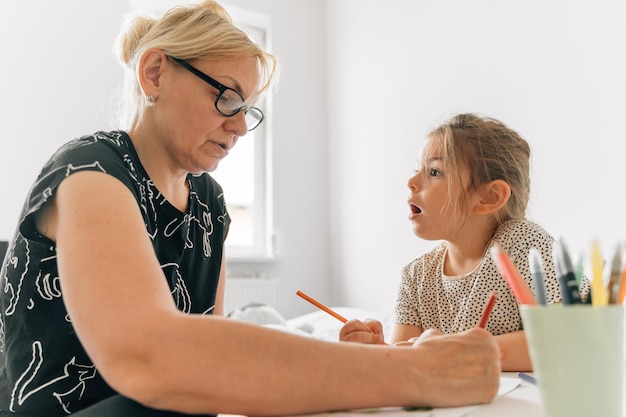 Mature woman granny with grandchild preschool girl drawing together at home