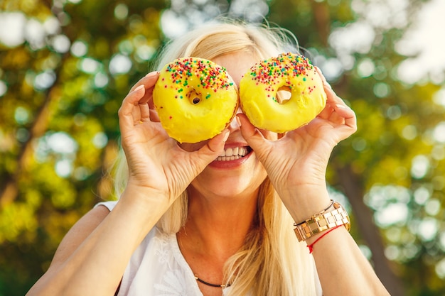 Mature woman having fun relaxing at the park hiding her face behind two delicious donuts