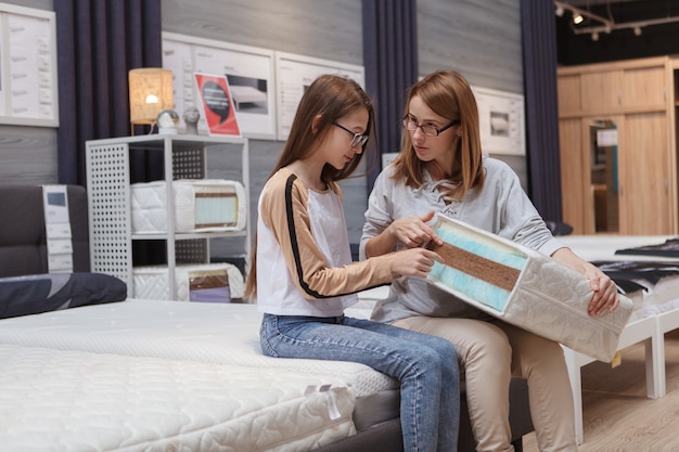 Mature woman and her daughter examining orthopedic mattress sample, shopping for furniture