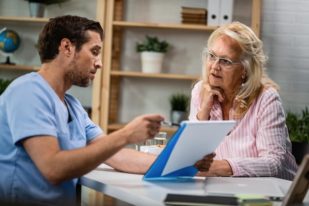 Photo mature woman and her doctor going through medical documents during the appointment at doctor's office focus is on woman