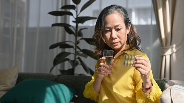 Mature woman holding holding pill and glass of fresh water Elderly healthcare medication concept