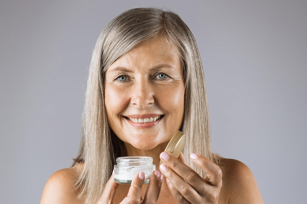 Mature woman holding jar with face cream in studio