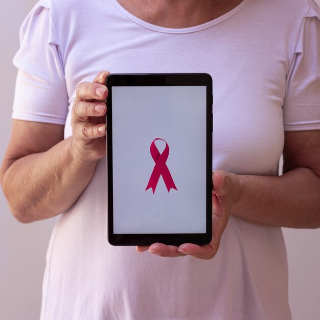 Mature woman holding tablet with a pink ribbon. Breast Cancer Awareness Month with tech image.