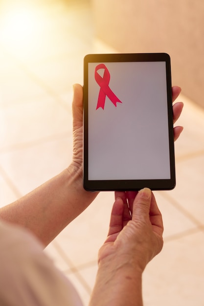 Mature woman holding tablet with a pink ribbon. Breast Cancer Awareness Month with tech image.