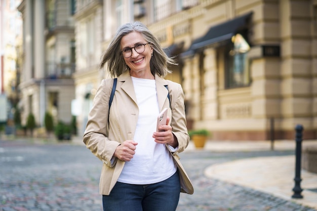 Foto donna matura tiene il telefono in piedi nella vecchia città europea concetto di felicità negli anziani